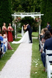 Newly married couple kissing while walking down the ceremony aisle after their wedding ceremony as guests celebrate around them