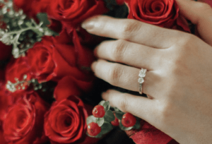 Hand wearing an engagement ring holding or surrounded by roses in a romantic engagement styled photograph.