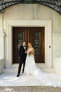 Newlywed couple standing at the historic front entrance of Evergreen Museum & Library during their wedding day portraits.
