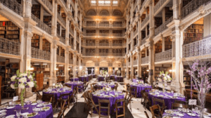 Elegant round dinner tables with purple linens and glowing string lights inside George Peabody Library during a romantic wedding reception.